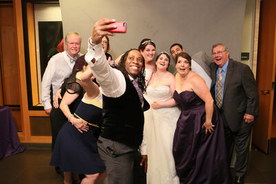 Wedding couple posing with guests at their reception, all smiling and dressed up.
