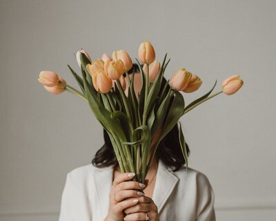 Woman holding a bouquet of tulips in front of her face, creating a minimal and elegant aesthetic.