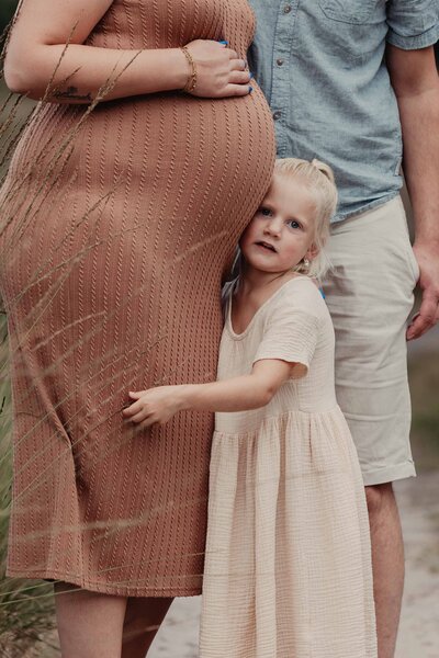 Meisje tegen de buik van mama aan waar haar baby broertje in zit tijdens de zwangerschapsshoot in zwartsluis