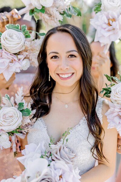 A bride smiles surrounded by bouquets of flowers