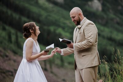 Bride laughs as groom puts ring on her finger during Maroon Bells intimate wedding ceremony.