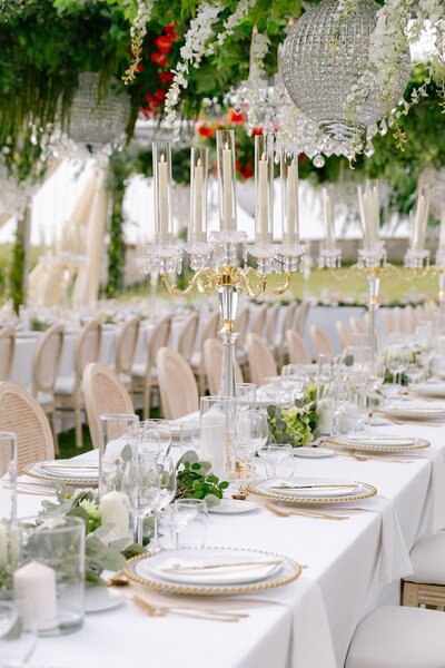 White wedding tables with opulent hanging florals, chandeliers, and greenery
