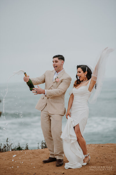 groom popping champagne while bride smiles
