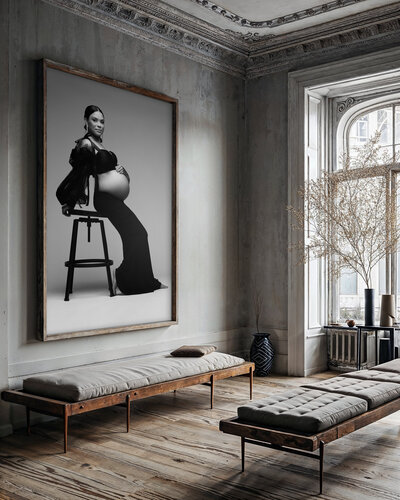 A beautiful expecting mother in a black gown and sheer black sleeves, elegantly seated on a black stool against a minimalist gray background. The confident pose showcases her glowing beauty and sophistication. Captured by DFW maternity photography Lindsay Walden.