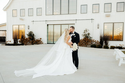 A bride and groom kissing in front of a grand, white barn venue.
