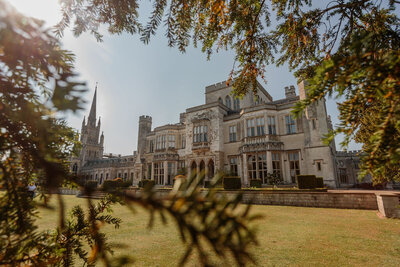 Elegant rear view of Ashridge House, a stunning historic estate with grand architecture, large windows, and intricate stone details. The beautifully manicured gardens in the foreground complement the stately exterior, with lush greenery and blooming flowers adding to the charm.