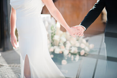 denver wedding photographer captures detail shot of bride and groom holding hands and walking through their outdoor wedding venue in denver
