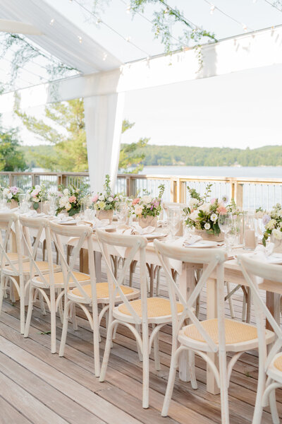 Wedding reception set up in a clear canopy with twinkly lights, white dishes, bronze cutlery, and light purple, pink, and white flowers
