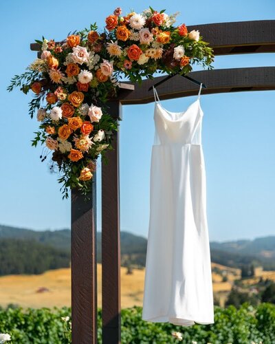 Wedding arch with wedding dress hanging and large floral installation by Flowers and Thyme.