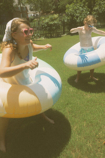 Two young kids standing in colorful inner tubes and laughing.