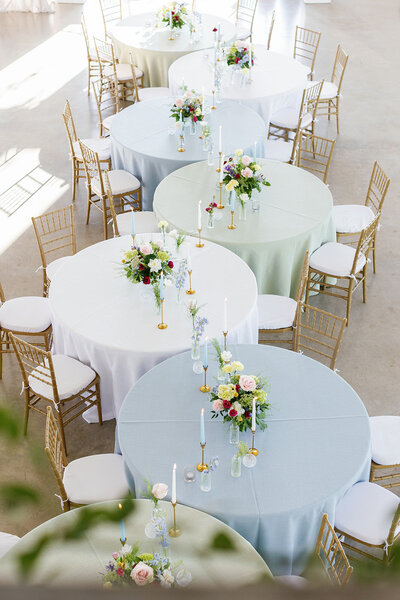 Serpentine wedding tables with blue, white, and green tablecloths with spring flowers and gold chivari chairs