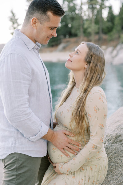 Mother cradling baby bump while standing at shoreline near Fresno