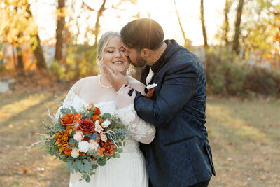 Groom kisses his bride's cheek as their eyes are closed and groom cups bride's jaw with his hand