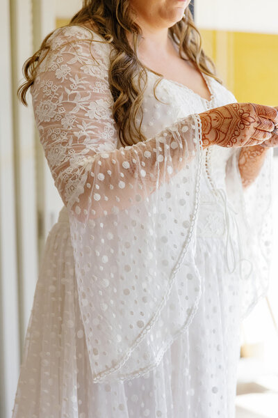 A close up of someone wearing a lace wedding dress with henna tattoos on their hands 