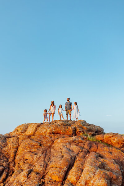 Family of five stand at the top of rocks and stare at the sunset while. holding hands with Overland Park KS photographers.