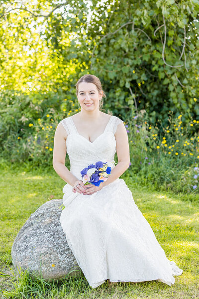 Bride sitting on rock holding bouquet looking at the camera