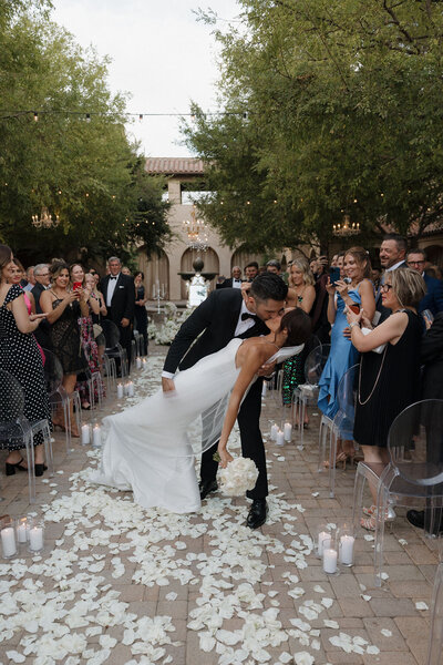 Bride and groom dip during ceremony recessional with rose petals and candles in the aisle