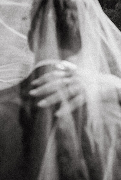 Black and white blurry photo of bride's hand on groom's shoulder underneath her veil