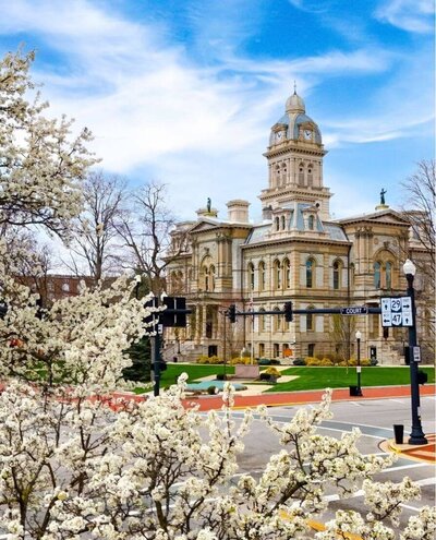 The historic Shelby County Courthouse in Sidney, OH, surrounded by blooming trees, representing the community Black Bear Roofing & Exteriors proudly serve with expert roofing and exterior services.
