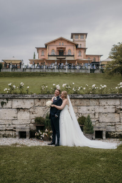 Bride and groom stand with distance before their wedding venue outside.