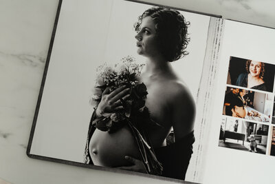 A black and white maternity portrait of a woman in an open photo album, holding a bouquet of flowers close to her chest, with a contemplative expression.