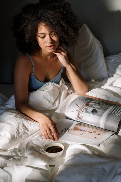 Woman sits in bed  reading a magazine over her morning coffee