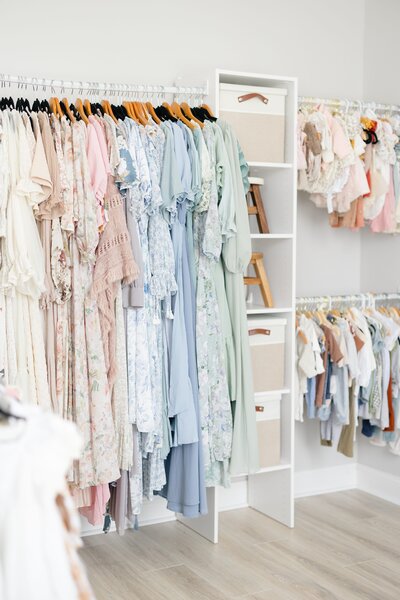 A row of beautiful light colored dresses hanging on a rack in front of a window