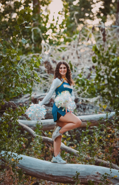girl in cheerleader uniform with pom-pons standing on a tree branch