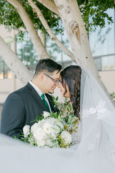 Groom faces forward, bride with back turned, dress train flowing gracefully on the grass as they share a gaze, a timeless moment of connection.