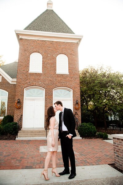 Newlyweds wearing formal wear sharing a quick kiss on the sidewalk in downtown Franklin