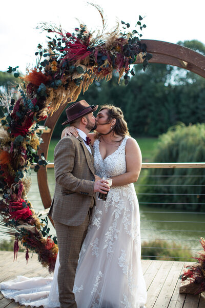Bride and groom under flower arch kissing