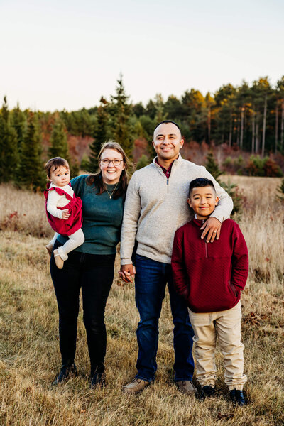 beautiful family with two kids standing in a field of Christmas Trees during their mini family session