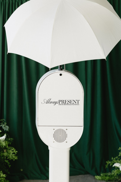 View of Always Present photo booth from behind showing brand decal, set against an emerald green velvet backdrop.