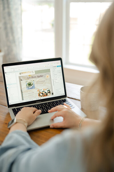 Woman sitting at a wooden table designing a custom Showit website on her Macbook Pro