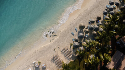 Drone shot of a Mexico beachfront wedding ceremony setup with chairs, umbrellas, and waves rolling onto the sand.