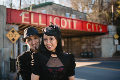 A couple standing behind each other smiling in front of a red bridge.