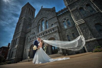 Wedding couple in front of Saint Patrick Church with veil blowing in wind.