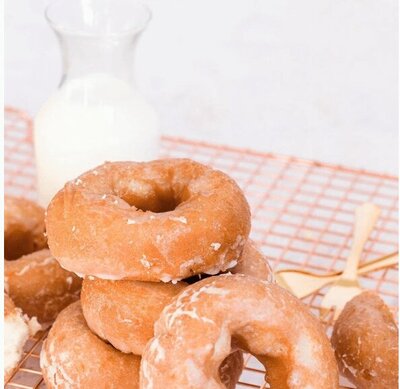 Donuts on a plate with a glass of milk in the background, all sitting on a checkerboard tablecloth