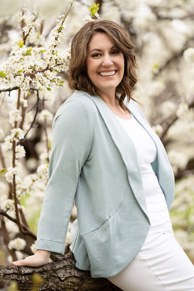 Photograph of Amanda Gibson award-winning and accredited newborn photographer wearing a blue and white outfit in the white Cherry Blossoms in Burlington, Ontario