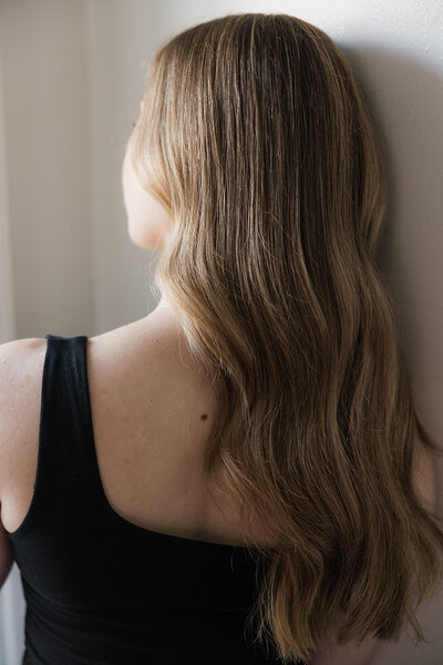 woman with dirty blonde hair in undone waves faces away from the camera in a black tank top
