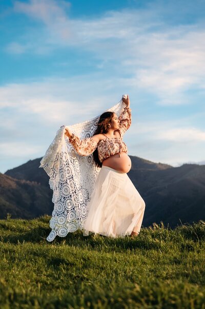 pregnant mom looking into sun with mountains in background