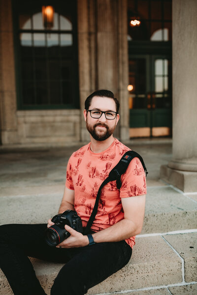 A man smiles while holding a camera