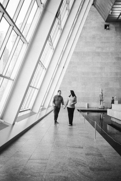couple holding hands while she touches her pregnant belly and walking down the sidewalk indoors