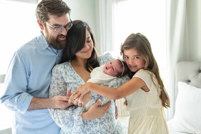 Family of four smiles while gathered closely around their newborn baby during an in-home session.
