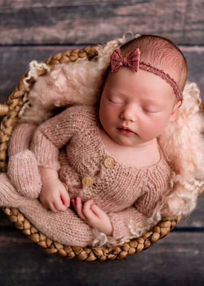 Studio newborn portrait by Stamford CT photographer showing baby girl in dusty rose knit outfit and matching headband in woven basket