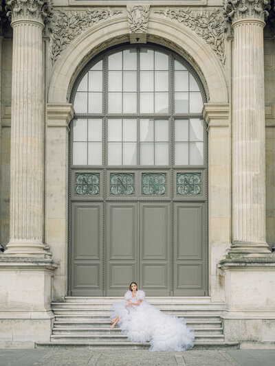 a woman in a large tulle dress sitting on some steps at the louvre in paris