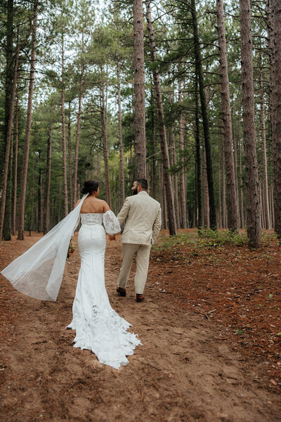 bride and groom walking through tall pine trees holding hands