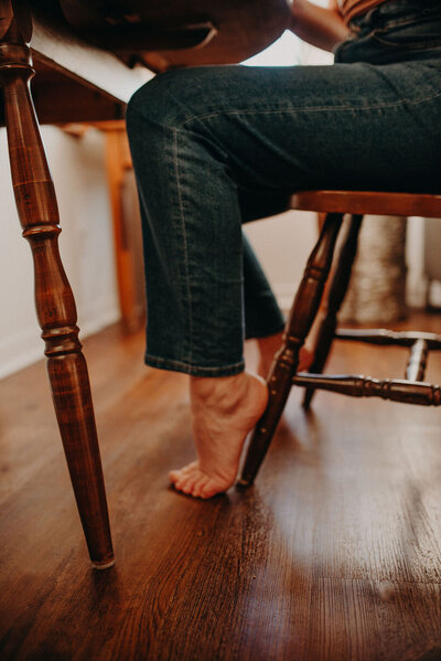 A woman sits at a table, her feet perched against the chair.