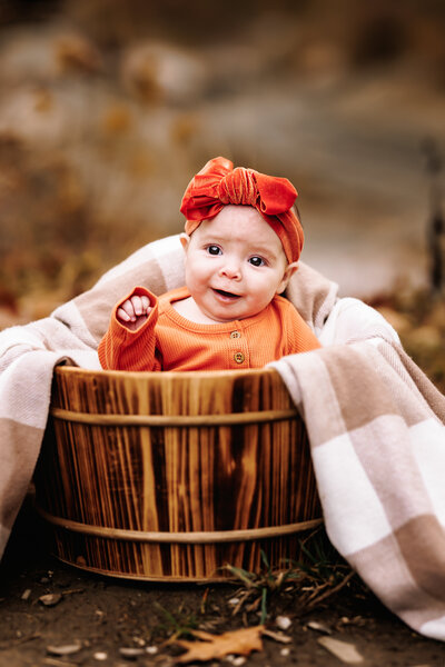 Adorable baby girl  cozied up in a wooden bucket on a crisp fall day