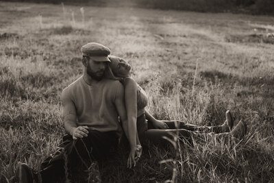 An aesthetic black and white photo of a couple during their photoshoot. They are back to back sitting in a field.